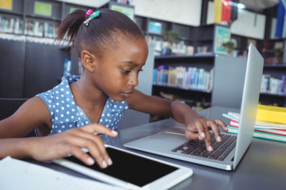 Girl focused on studying with a laptop in a library, symbolizing the power of digital education that CADED brings to vulnerable communities as a true hero.