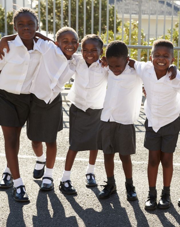 Group of five children in school uniforms hugging and smiling in a courtyard, representing the educational mission of the CADED foundation, a non-profit organization
