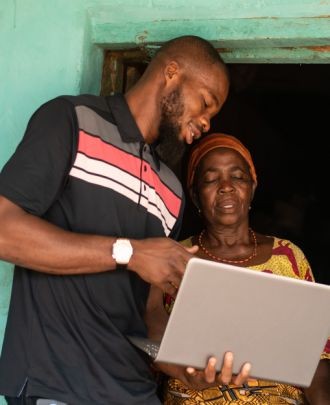 Young man teaching an elderly woman to use a laptop, symbolizing the CADED foundation's commitment to education and digital access for vulnerable communities